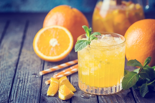 Glass jar of fresh orange juice with ice and fresh fruits on dark table