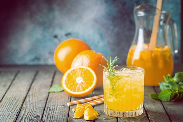 Glass jar of fresh orange juice with ice and fresh fruits on dark table