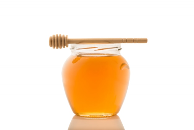 Vaso di vetro pieno di miele e bastone di legno su di esso isolato su uno sfondo bianco