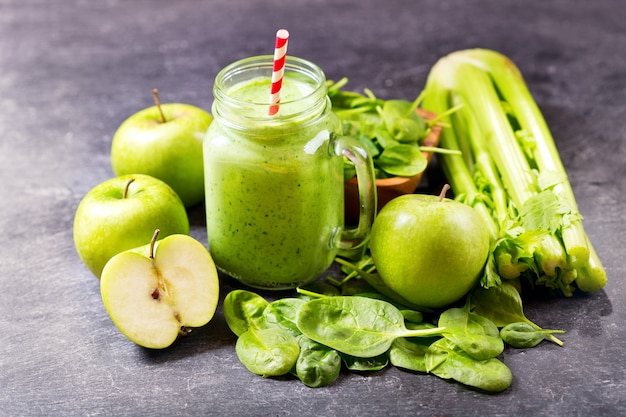 Glass jar of green juice smoothie with spinach, apple and celery on dark 