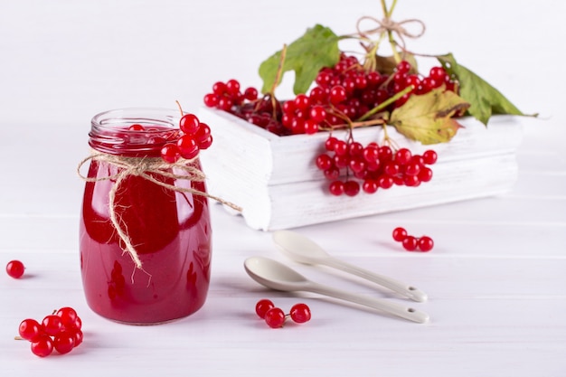 Glass jar of homemade viburnum jam with fresh berries  on white table.