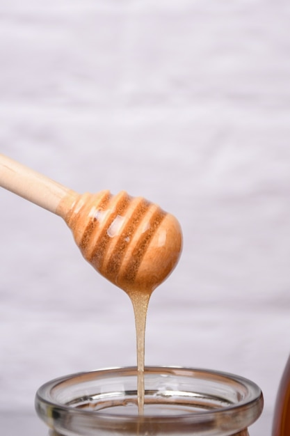 Glass jar and honey dripping from dipper on white background Copyspace