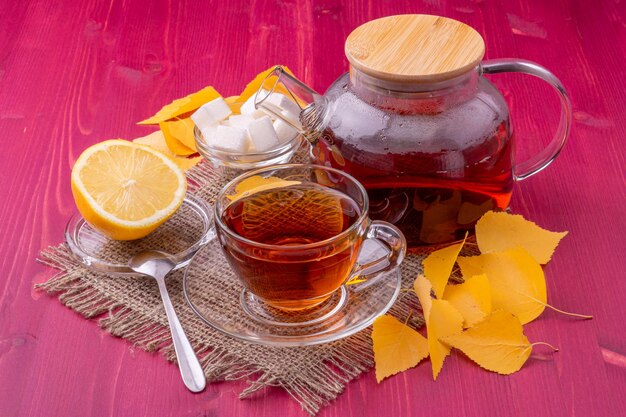 A glass jar of honey and a glass of lemon juice with a wooden spoon next to it.