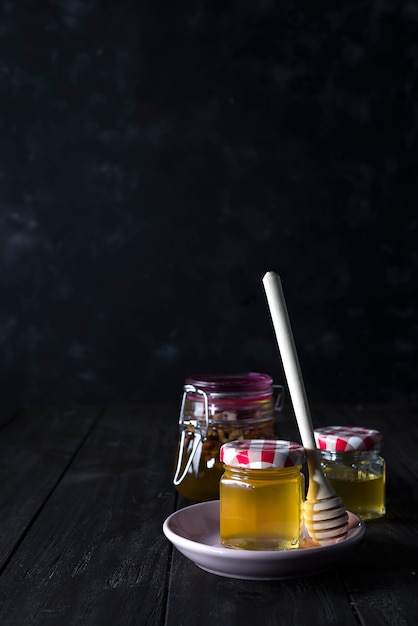 Glass jar of honey and stick on a ceramic plate on a dark concrete background , copy space