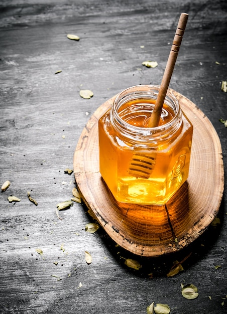 Glass jar honey with spoon on a wooden trunk on black rustic background