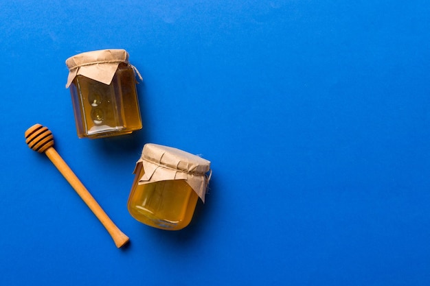 Glass jar of honey with wooden drizzler on colored background Honey pot and dipper high above Top view copy space