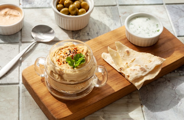 Glass jar of hummus, traditional jewish, arabian, middle\
eastern food from chick-peas with deeps and with pita flatbread on\
ceramic tile background. close up, selective focus