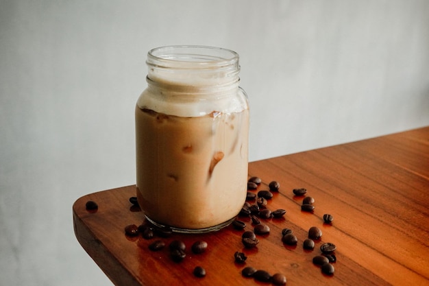 A glass jar of iced coffee with a brown drink on a wooden table.