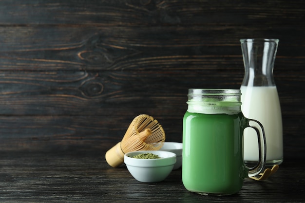 Glass jar of matcha latte and accessories for making on wooden background