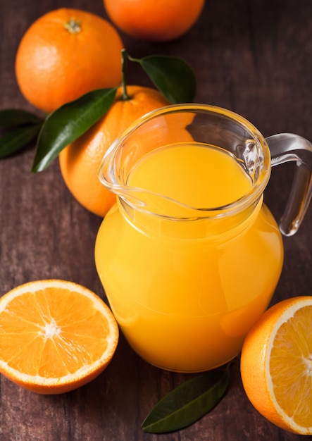 Glass jar of organic fresh orange juice with raw oranges on dark wooden background