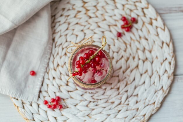 Glass jar of red currant soda drink on white wooden table