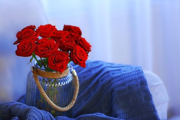 Glass jar of red roses on sofa