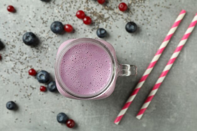 Photo glass jar of smoothie, ingredients and straws on gray textured table