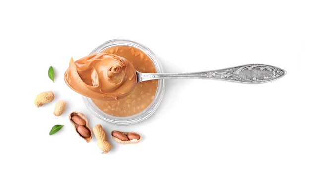 Glass jar and spoon full of peanut butter isolated on white