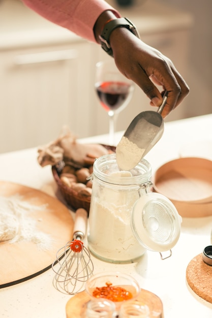 Glass jar standing on the table and hand of man taking flour from it with a help of scoop