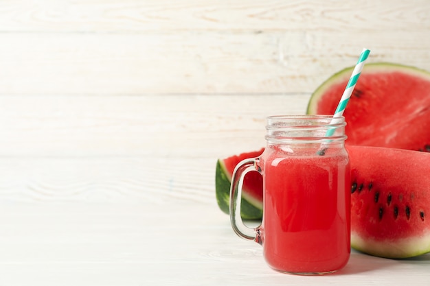 Glass jar of watermelon juice and slices on white wood