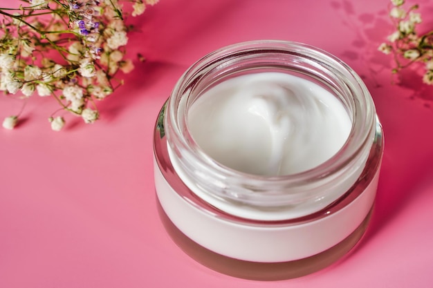 Glass jar and white cap with body cream on pink background. Cosmetic product for skin care. Transparent jar with face. High quality photo