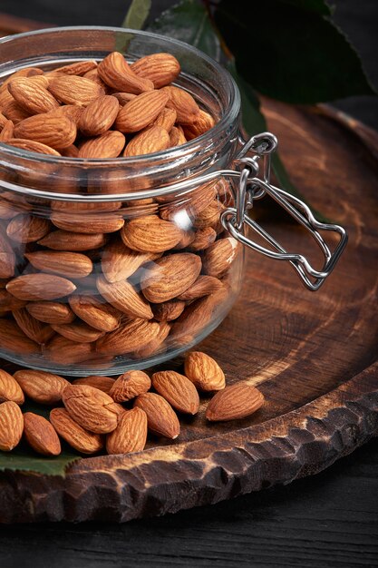 Glass jar with almond on wooden board, black background. Vitamin food