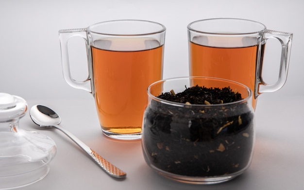 A glass jar with black tea leaves, two cups of tea and spoon, tea time for two