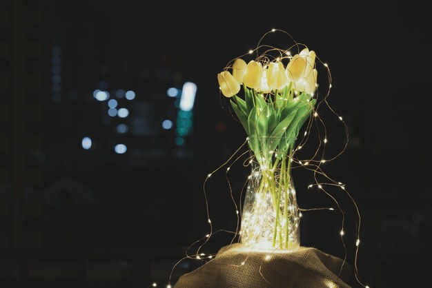 A glass jar with a bunch of tulips surrounded with a string of lights with golden warm lights glowing