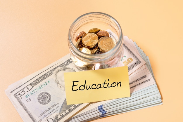 Glass jar with coins and banknote of 50 dollars with education label. Financial concept.