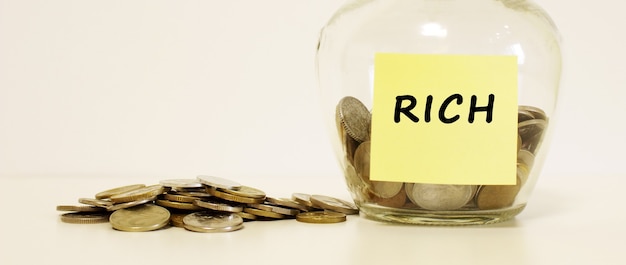 Glass jar with coins for savings. The inscription RICH on the note paper. Financial concept.