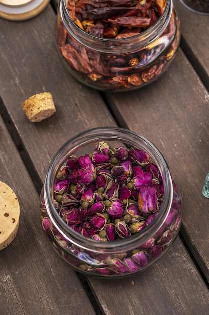 Glass jar with cork lids filled with dried tea roses on unvarnished dark wood planks