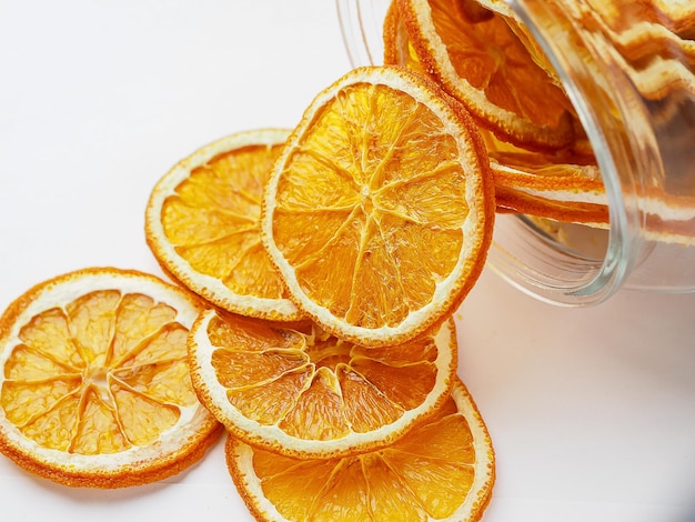 Glass jar with dried oranges on white background.