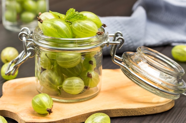 Glass jar with green gooseberries on board. Gray napkin. Dark wooden background. Top view