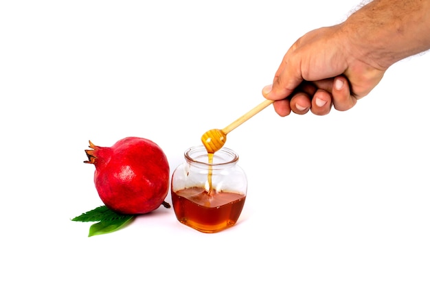 Glass jar with healthy organic thick honey and a wooden stick pomegranate on a white surface Space for text