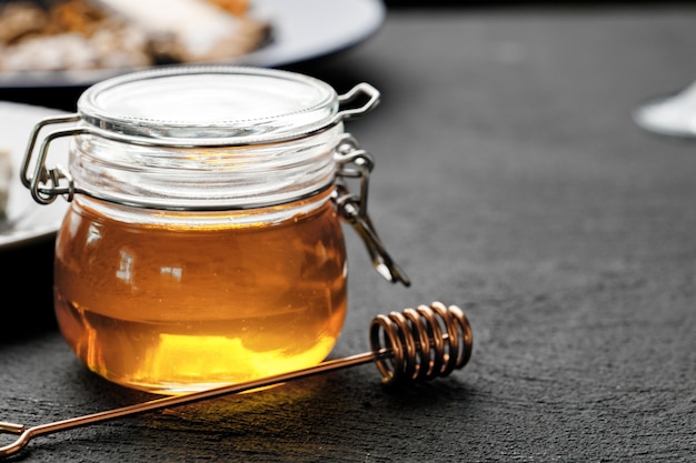 Glass jar with honey on black table close up