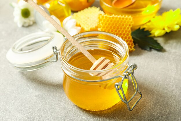 Glass jar with honey, dipper, honeycombs and flowers on grey