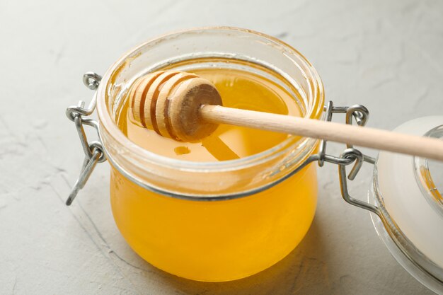 Glass jar with honey and dipper on white background