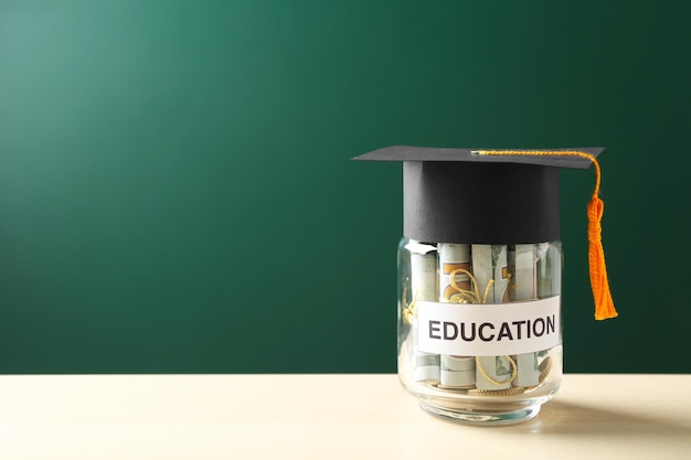 Glass jar with money for education on wooden table against green background