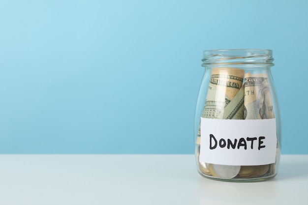 Glass jar with money and text Donate on white table