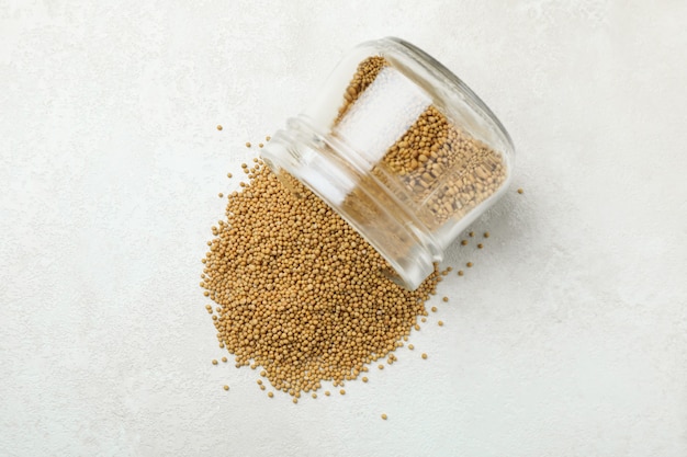 Glass jar with mustard seeds on white textured background