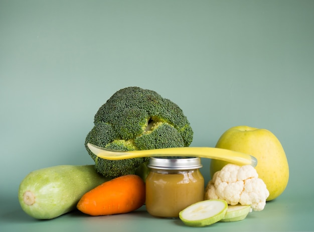 Glass jar with natural baby food on the table: vegetable puree with zucchini, broccoli, cauliflower; selective focus