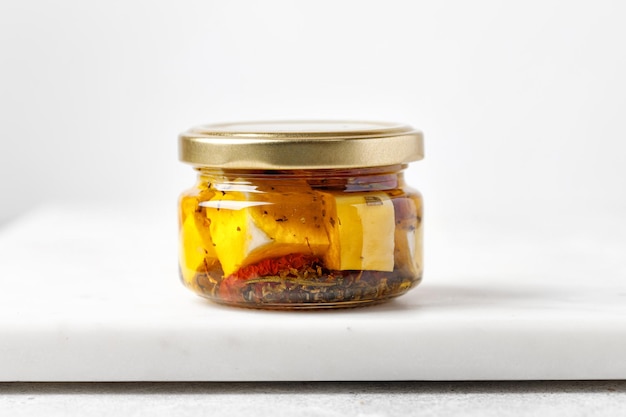 Glass jar with nature feta cheese and tomatoes in olive oil Product on marble board