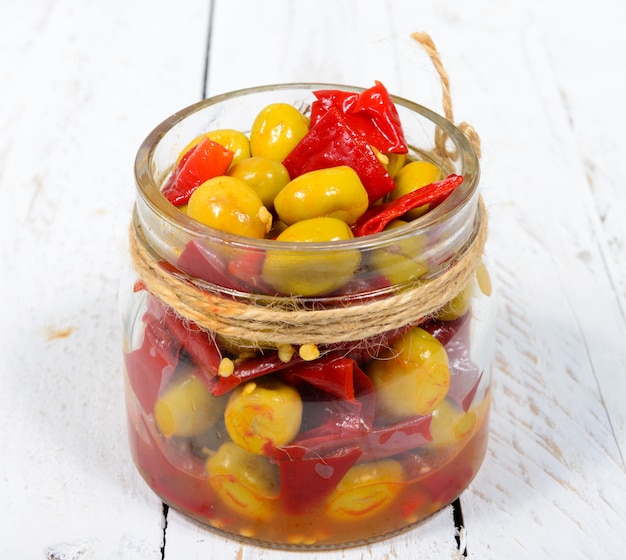 Glass jar with olives and peppers on white table