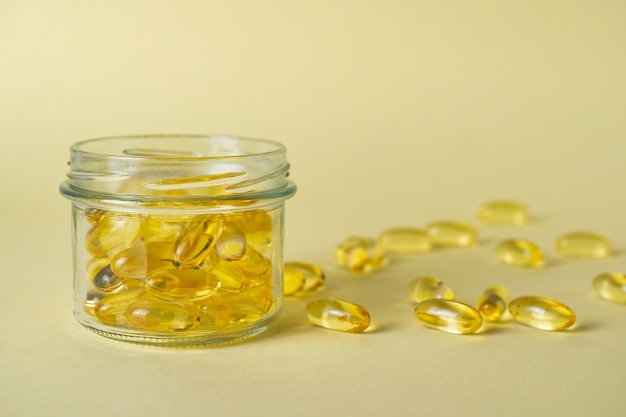 Glass jar with omega 3 fish fat oil capsules on yellow background