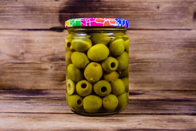 Glass jar with pickled green olives on rustic wooden table