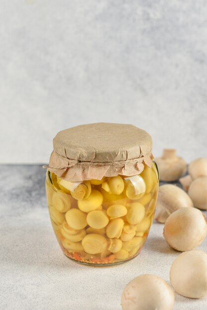 Glass jar with pickled mushrooms champignons on a light background. Chapminions on white background with copy space.