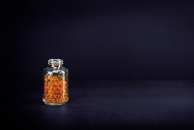 A glass jar with pills of bright orange yellow color on a purple background.