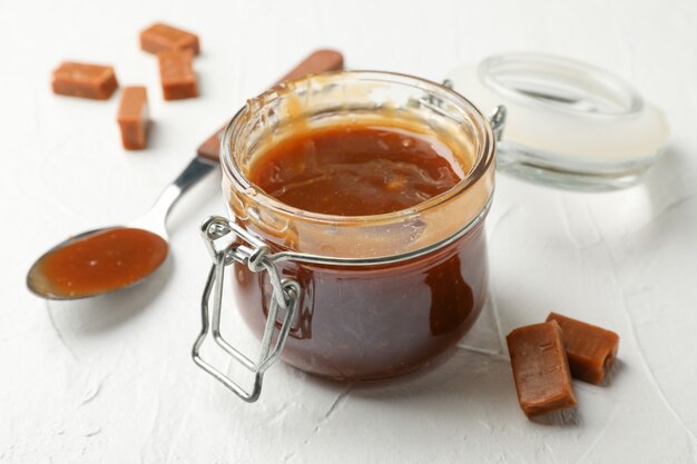 Glass jar with salted caramel and candies on white space, close up