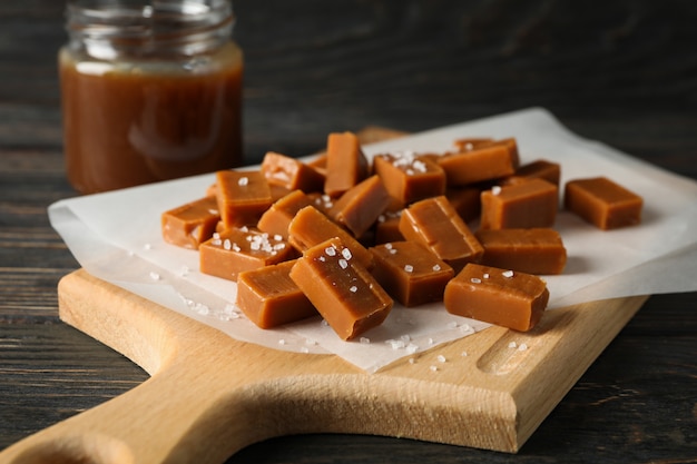 Glass jar with salted caramel and candies on wooden space, close up