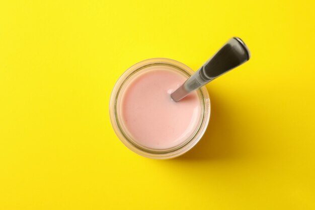 Glass jar with spoon and yogurt on yellow background