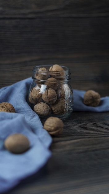 glass jar with walnuts surrounded by a blue kitchen towel on a wooden background closeup