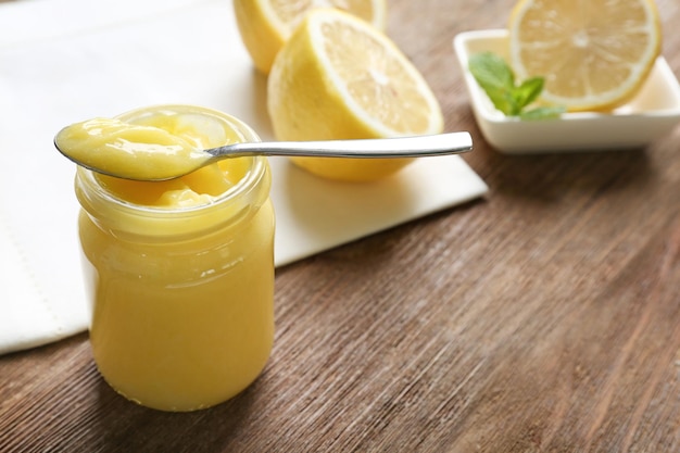 Glass jar with yummy lemon curd on wooden table