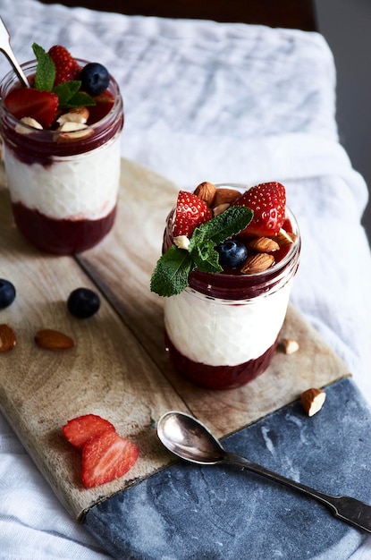 a glass jar of yogurt with berries on it sits on a cutting board