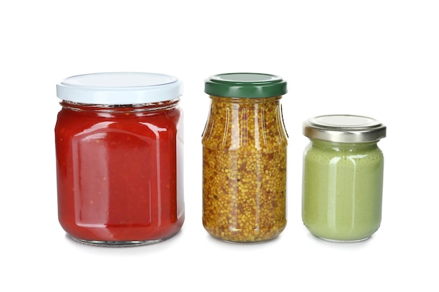 Glass jars of different sauces isolated on white